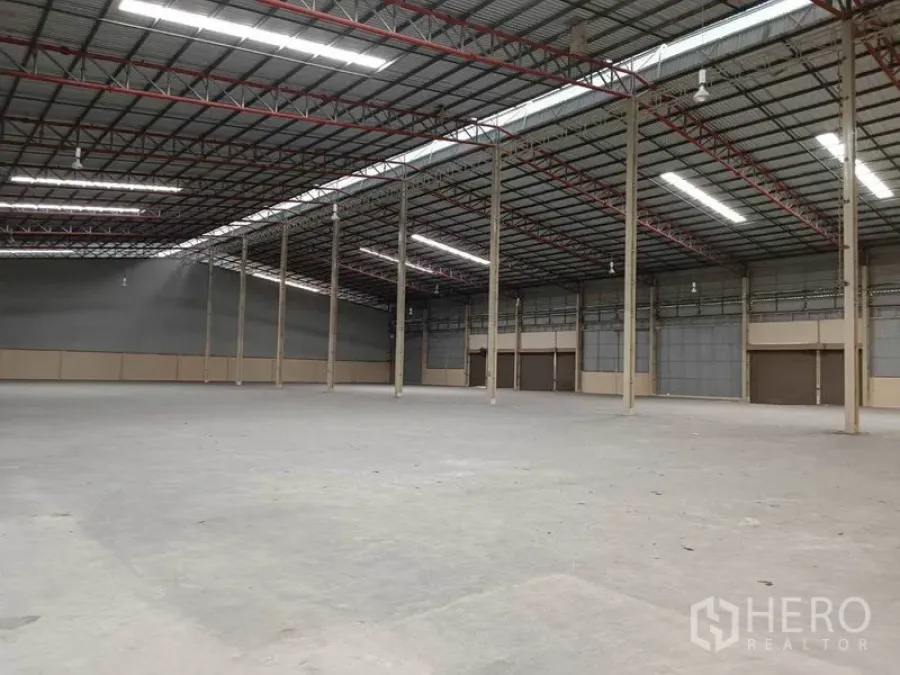 Factory for rent in Samut Prakan - Open factory interior with steel structure, ventilated wall panels, smooth concrete flooring and several large roll-up loading doors.