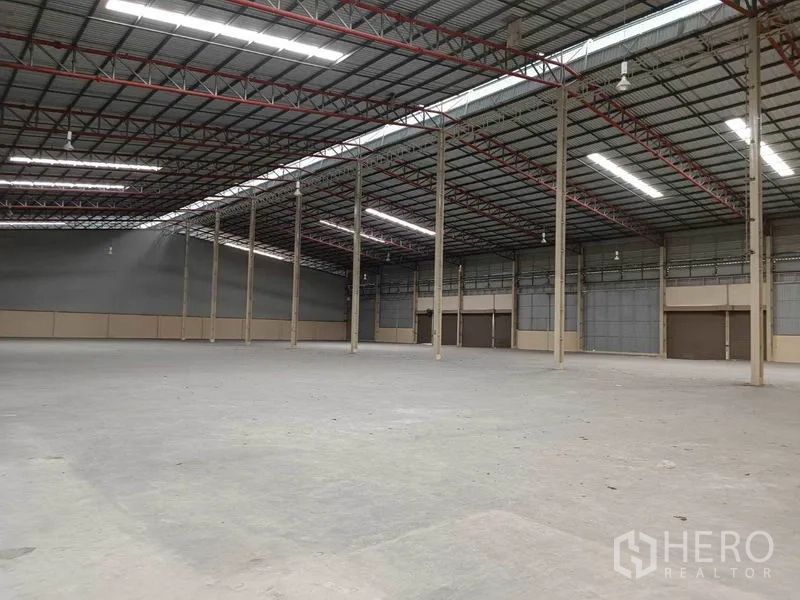 Factory for rent in Samut Prakan - Open factory interior with steel structure, ventilated wall panels, smooth concrete flooring and several large roll-up loading doors.