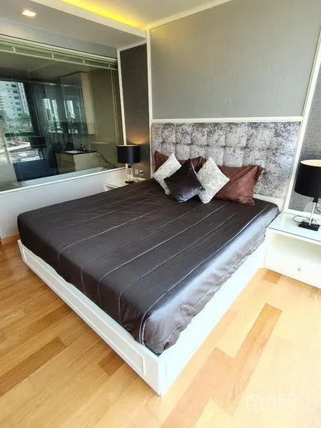 Condominium for rent in Watthana, Bangkok - Cozy bedroom with king bed, upholstered headboard, wood floors and glass wall to the bathroom.