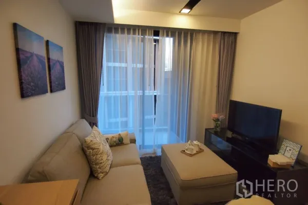 公寓 出租在Pathum Wan, Bangkok - 温馨客厅，沙发与脚凳，落地纱帘与大窗采光。