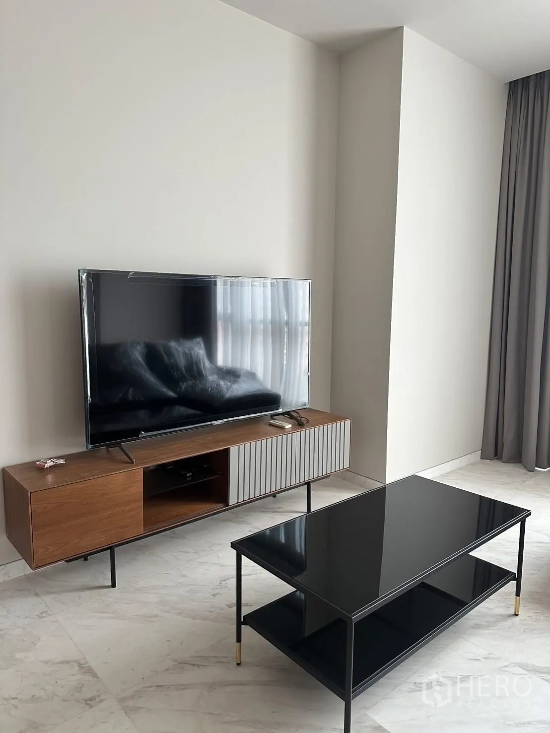 คอนโด for rent or sale in Watthana, Bangkok - มุมทีวีในห้องนั่งเล่นพร้อมโต๊ะกลางกระจกเงาบนพื้นลายหินอ่อน.