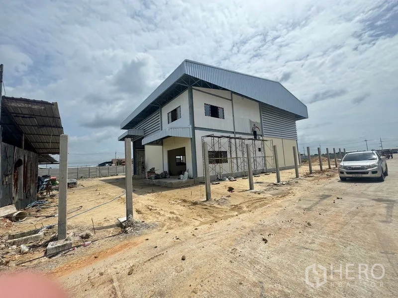 Warehouse for rent in Mueang Samut Prakan, Samut Prakan - Wide exterior of a modern two‑storey warehouse with metal roof and perimeter posts along a paved road.