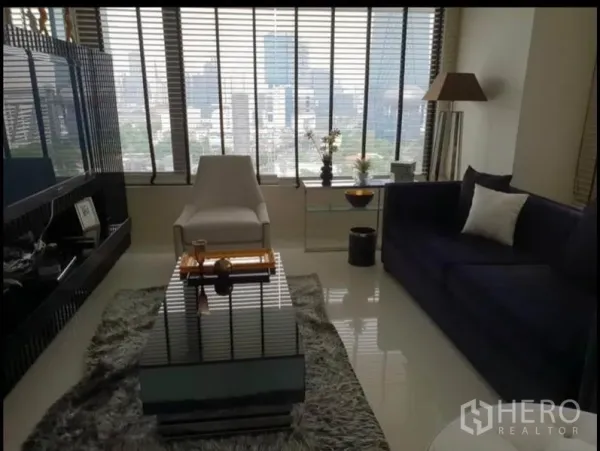 Condominium for rent in Sathon, Bangkok - Modern living room with floor-to-ceiling windows, city skyline view, sofa and armchair.