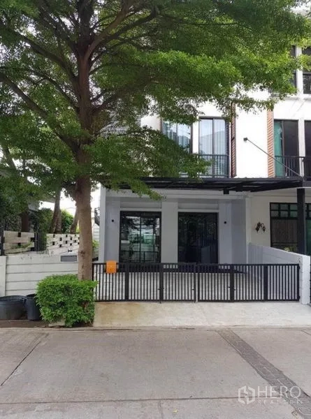 Townhouse for rent in Suan Luang, Bangkok - Front view of the townhouse exterior with a black gate and covered parking.