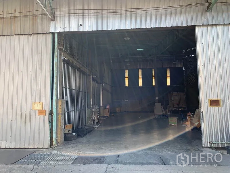 Warehouse for rent in Mueang Pathum Thani, Pathum Thani - Industrial warehouse entrance with roller doors, ventilated brick walls, open floor space and stacked cartons.