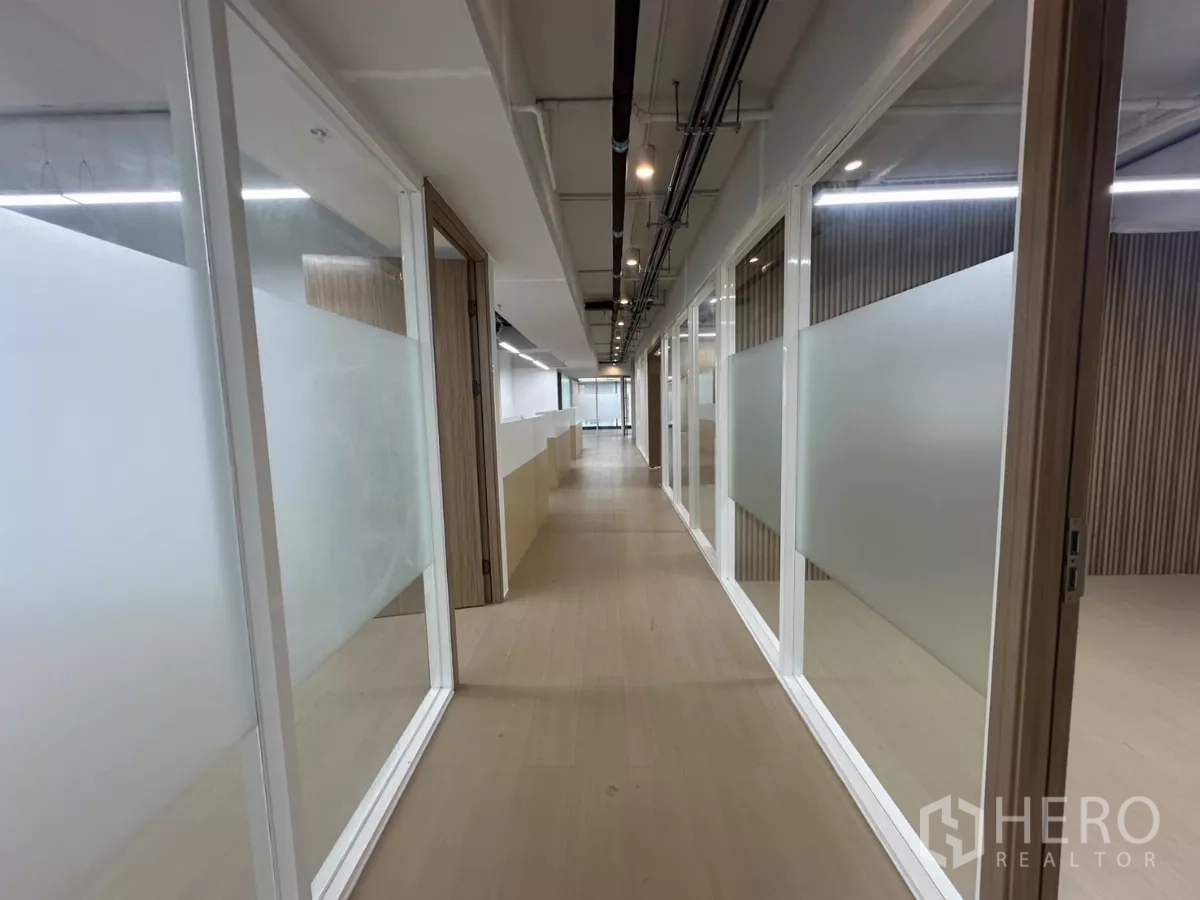 办公空间 出租在Watthana, Bangkok - 走廊两侧为玻璃隔间与线性灯。