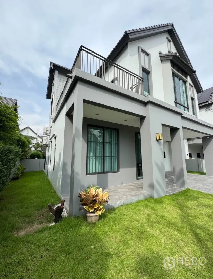 Detached House for rent or sale in Lat Krabang, Bangkok - Side exterior of the house with balcony above, covered patio, and landscaped green lawn along the boundary.