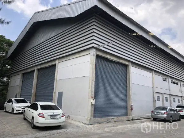 Warehouse for rent in Khlong Sam Wa, Bangkok - Corner view of a modern industrial warehouse in Khlong Sam Wa with high metal-clad roof, multiple roller shutter doors and on-site parking.