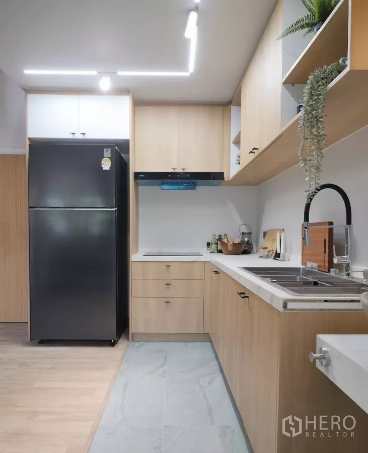 Townhouse for rent in Watthana, Bangkok - Modern L-shaped kitchen with light wood cabinetry, black refrigerator and sleek lighting.