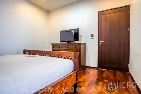 Condominium for rent or sale in Watthana, Bangkok - Cozy bedroom with wooden bed, dresser and TV on warm hardwood flooring.