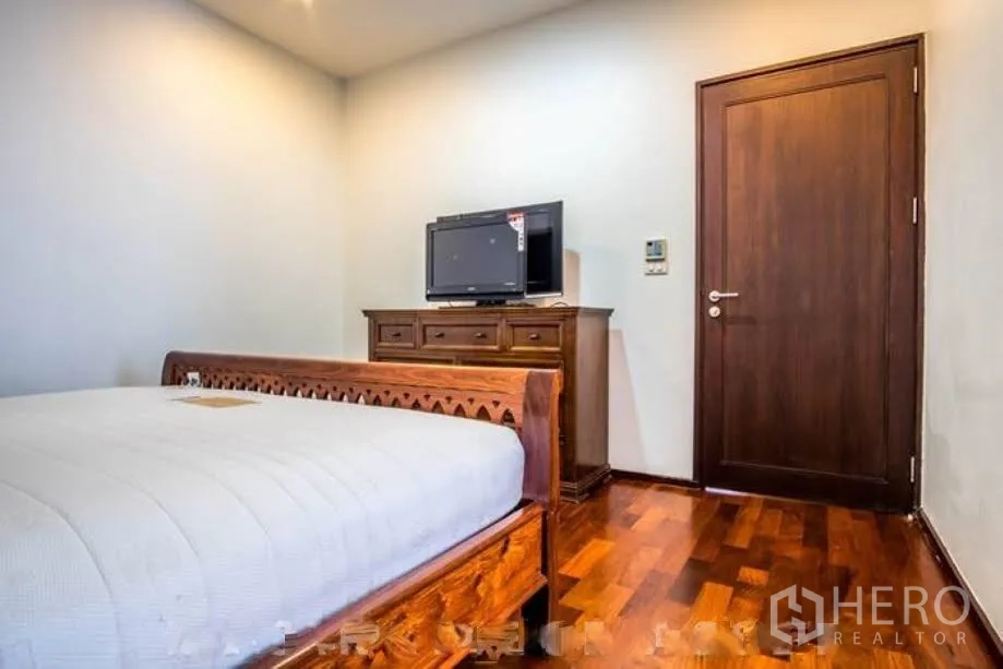 Condominium for rent or sale in Watthana, Bangkok - Cozy bedroom with wooden bed, dresser and TV on warm hardwood flooring.