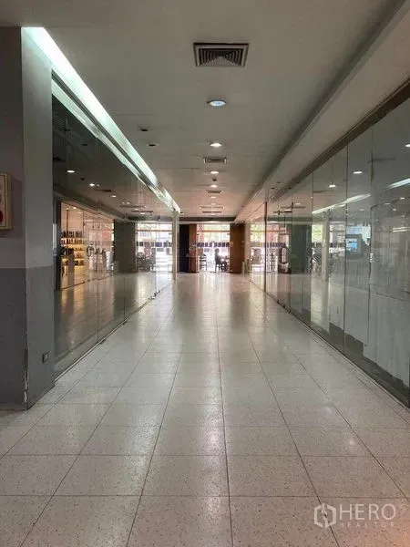 Retail Space for rent - Long mall hallway with glass storefronts on both sides, recessed lighting and air-conditioning vents leading to the entrance.