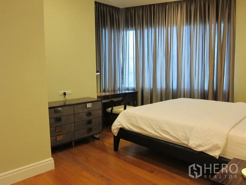 Condominium for rent in Khlong Toei, Bangkok - Bedroom corner showing large curtained windows, dresser and work desk.