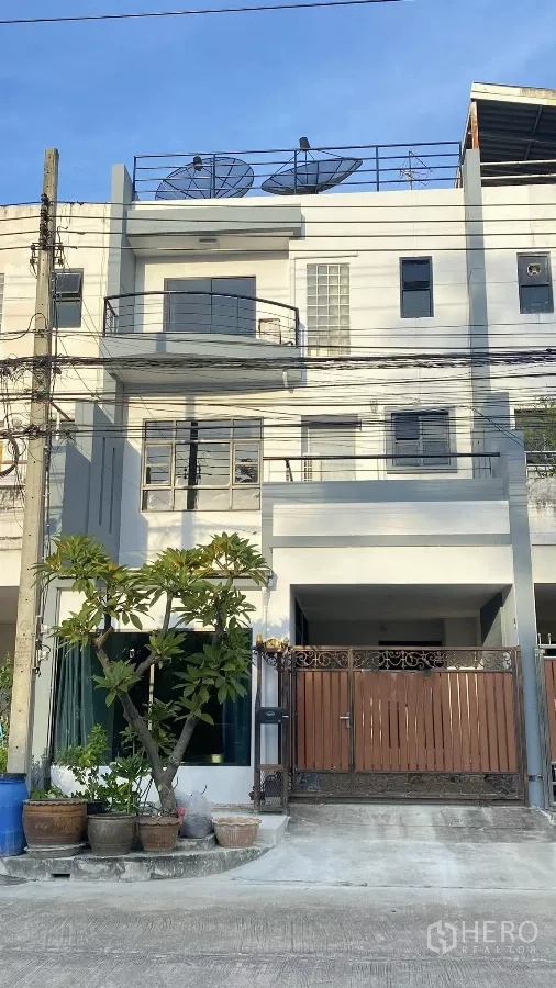 Home Office for rent in Bang Na, Bangkok - Three-storey home office facade with balconies, gated parking, rooftop dishes and potted plants.