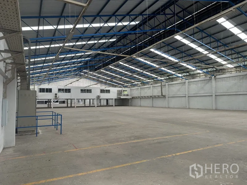 Factory for rent in Nonthaburi - Spacious factory hall with steel truss roof, skylights and a raised office block.