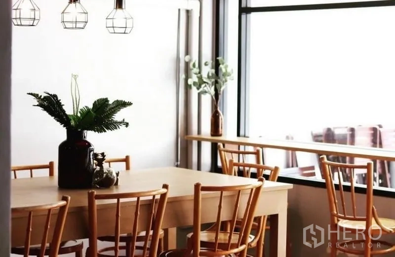 Townhouse for rent in Chatuchak, Bangkok - Bright dining space by a picture window with wooden chairs and cage lights.