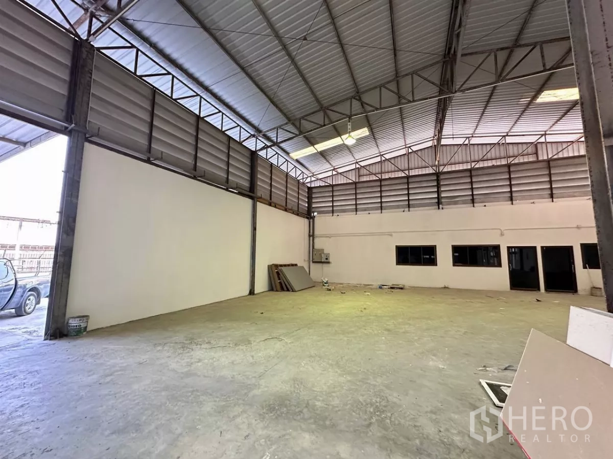 Factory for rent in Samut Prakan - High-clearance warehouse bay beside an office block with vehicle access.
