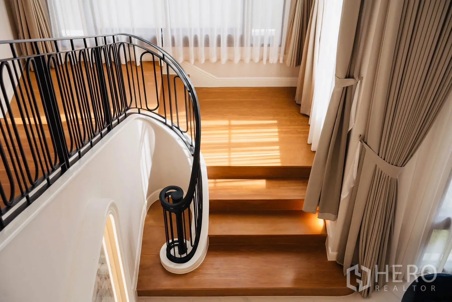Detached House for rent or sale in Bang Kapi, Bangkok - Wooden staircase with curved black metal balustrade and window drapes.