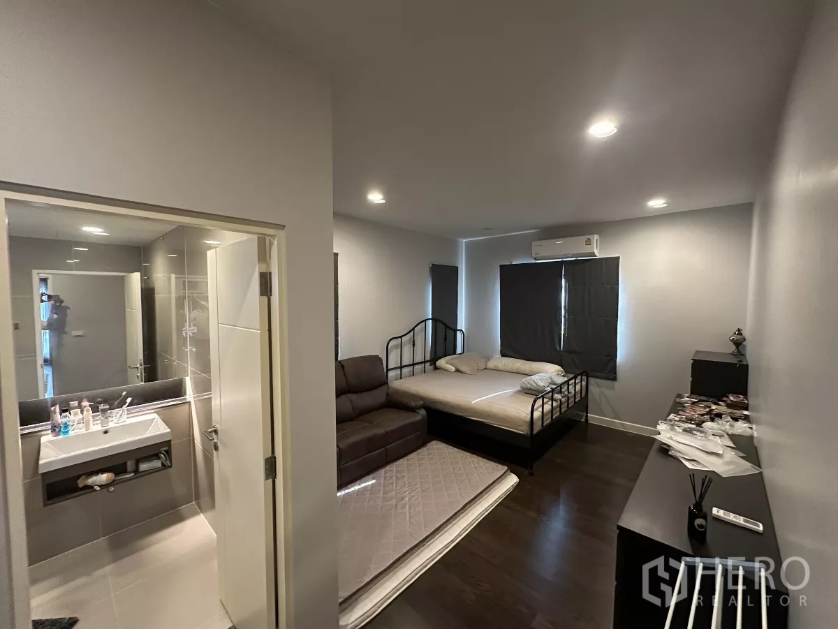 Detached House for rent or sale in Lam Luk Ka, Pathum Thani - Bedroom with entrance to an ensuite bathroom, bed and sofa, air conditioning and blackout blinds.