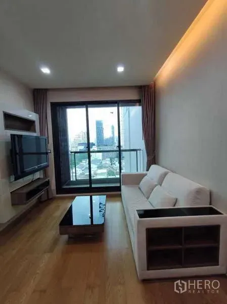 Condominium for rent in Bang Rak, Bangkok - Bright living room with sofa, wall-mounted TV and balcony city view.