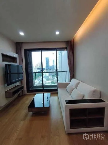 Condominium for rent in Bang Rak, Bangkok - Bright living room with sofa, wall-mounted TV and balcony city view.