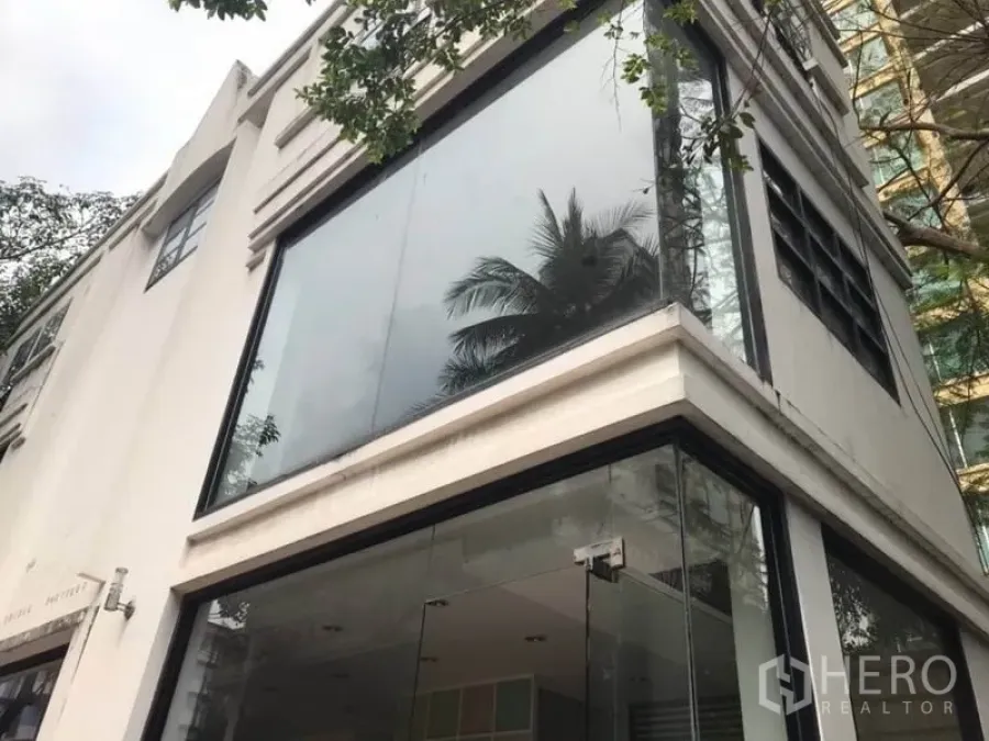 Retail Space for rent in Watthana, Bangkok - Modern corner retail building with double-height glass facade and tree reflections in the windows.