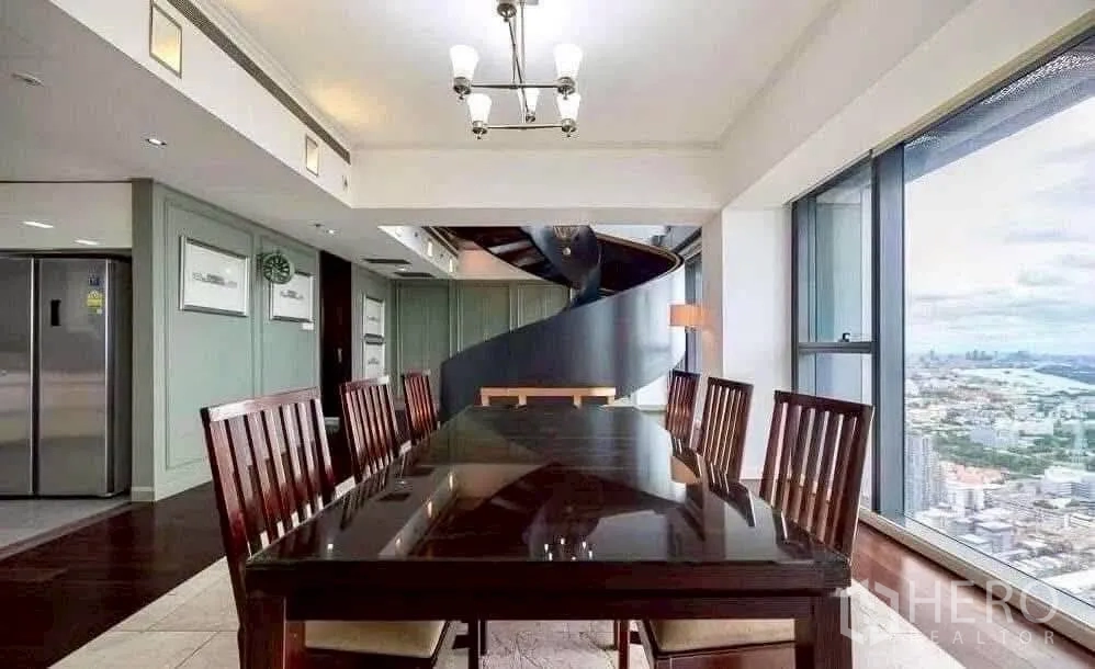 Condominium for rent in Sathon, Bangkok - Formal dining area beside floor-to-ceiling windows with a sculptural spiral staircase and skyline river views.