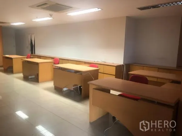 Office Space for rent in Sathon, Bangkok - Row of wooden workstations with red chairs under bright fluorescent lights on a tiled floor.