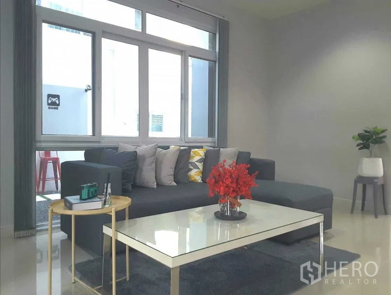 Detached House for rent in Lam Luk Ka, Pathum Thani - Cozy sitting area featuring a sectional sofa and glass-top coffee table near a window.
