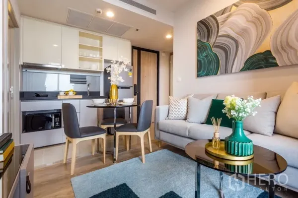 Condominium for rent in Khlong Toei, Bangkok - Modern open-plan living area with built-in kitchen, round dining table, and sofa with abstract art.