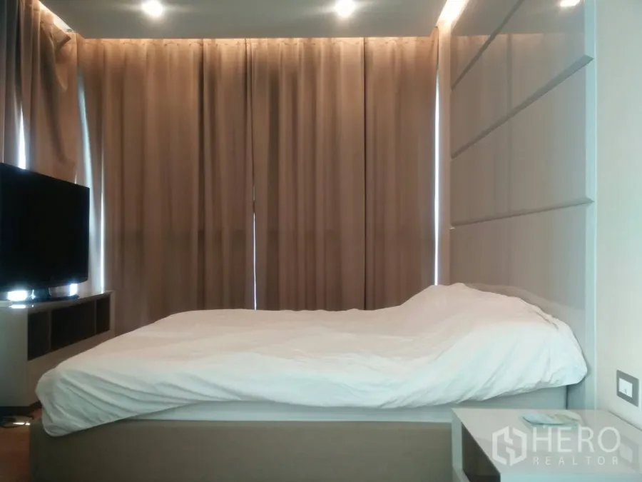 คอนโด ให้เช่าในRatchathewi, Bangkok - ห้องนอนมาสเตอร์พร้อมเตียง ผนังหัวเตียงบิลท์อิน ทีวี และผ้าม่านทึบแสงในคอนโดย่านกรุงเทพฯ