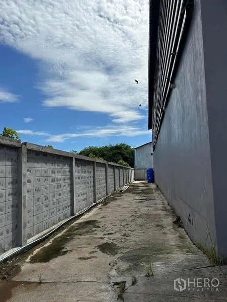 货栈 出售在Lat Lum Kaeo, Pathum Thani - 仓库旁边界围墙的后部通道，天空晴朗。