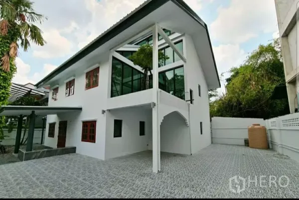Home Office for rent in Lat Phrao, Bangkok - Angled exterior showing glass corner pavilion, wide paved driveway and mature trees.