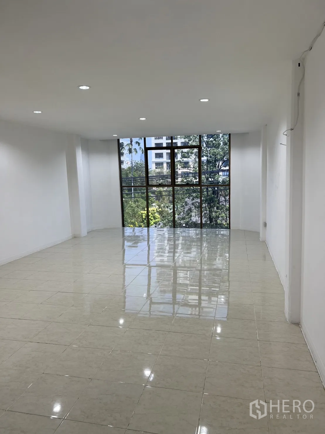 Shophouse for rent in Watthana, Bangkok - Bright upper-floor room with glossy tiles and a large window overlooking greenery.