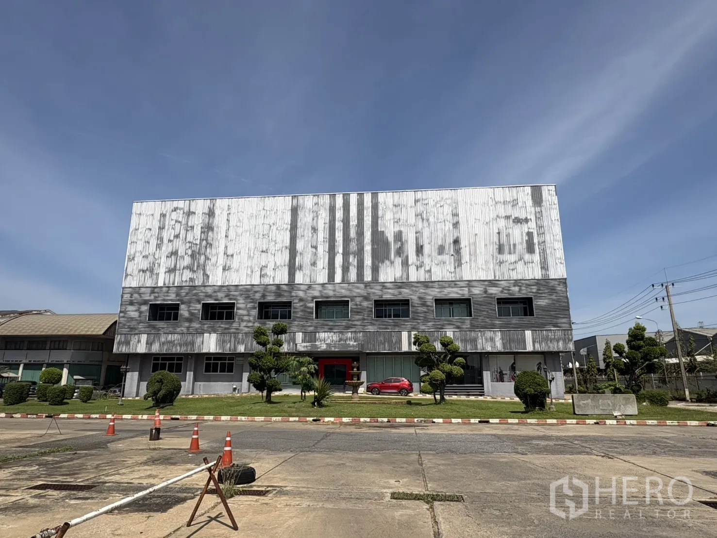 โรงงาน for rent in Lat Krabang, Bangkok - อาคารโรงงานเมทัลชีท 3 ชั้น มีหน้าต่างสำนักงาน สนามหญ้า และลานคอนกรีตกว้าง พร้อมกรวยจราจร ใต้ท้องฟ้าโปร่ง ในย่านลาดกระบัง กรุงเทพฯ
