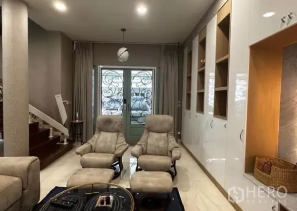 Townhouse for rent in Yan Nawa, Bangkok - Cozy lounge with reclining chairs, built-in storage wall, and decorative front doors near the staircase.