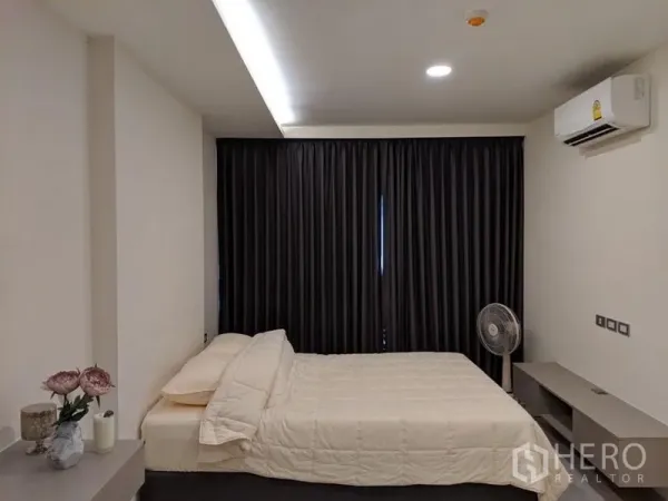 Condominium for sale in Khlong Toei, Bangkok - Minimalist bedroom with a queen bed, blackout curtains, recessed lighting and wall-mounted air conditioner.