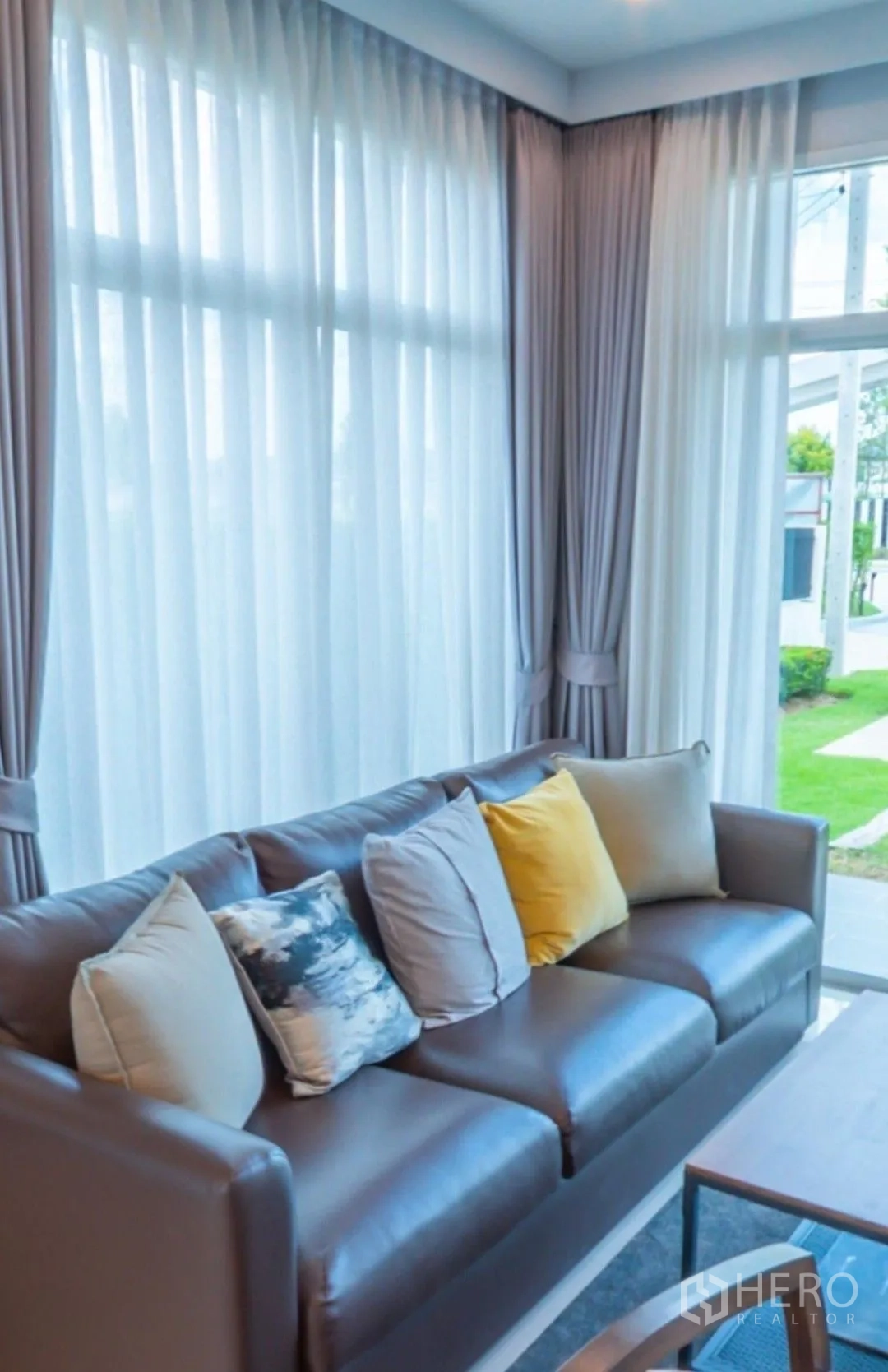 Detached House for rent in Lam Luk Ka, Pathum Thani - Close-up of the living room sofa beside full-height curtains and lawn outside.