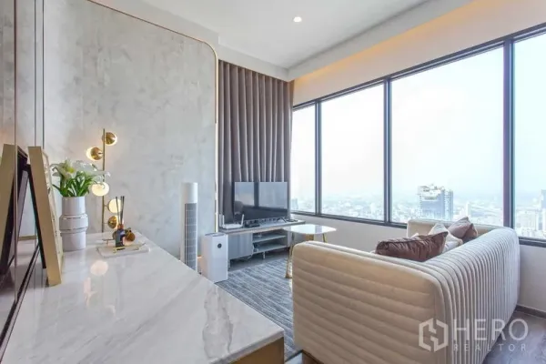 คอนโด ให้เช่าในWatthana, Bangkok - ห้องนั่งเล่นสว่างไสวพร้อมท็อปหินอ่อน โทนทอง และหน้าต่างบานใหญ่ชมวิวสกายไลน์กรุงเทพฯ