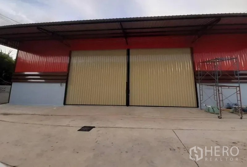 Warehouse for rent in Lam Luk Ka, Pathum Thani - Warehouse exterior with wide cream sliding doors, red cladding and a large concrete loading apron.