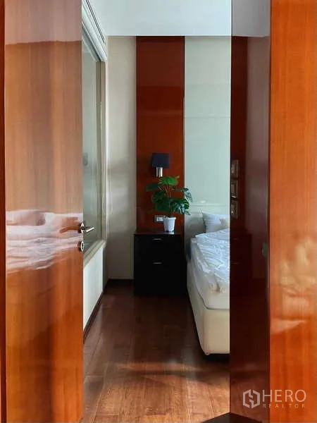 Condominium for rent or sale - Entrance to the bedroom with wooden doors, bedside table and indoor plant.
