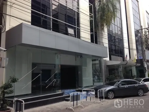 Office Space for rent in Bang Kapi, Bangkok - Modern glass-front office building entrance with car drop-off area on a Bangkok street.