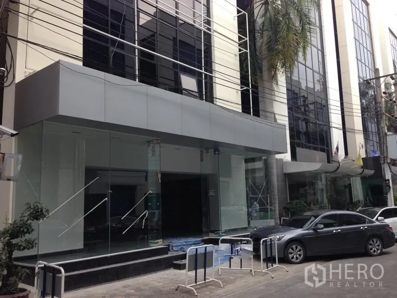 Office Space for rent in Bang Kapi, Bangkok - Modern glass-front office building entrance with car drop-off area on a Bangkok street.