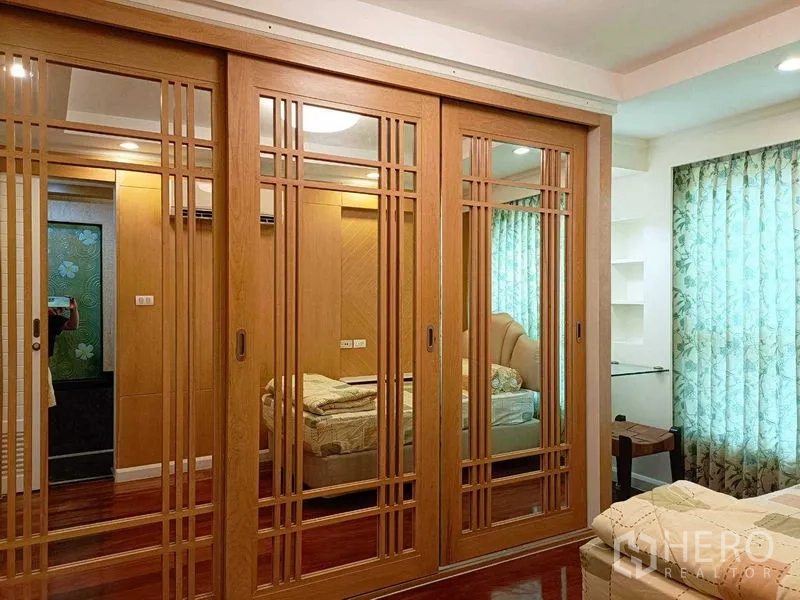 公寓 出租在Watthana, Bangkok - 卧室整面镜面木质移门衣柜，映出床与温暖木饰面。