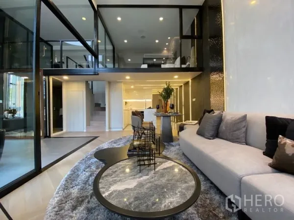 独立式住宅 出售在Watthana, Bangkok - 现代客厅，转角沙发与圆形茶几，开放式厨房上方为夹层