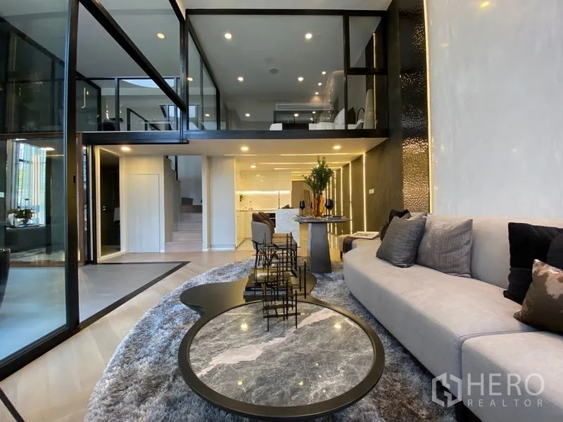 独立式住宅 出售在Watthana, Bangkok - 现代客厅，转角沙发与圆形茶几，开放式厨房上方为夹层