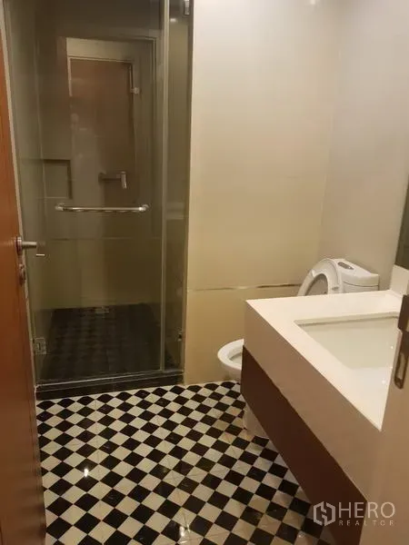 公寓 出租在Watthana, Bangkok - 浴室采用棋盘格地砖，玻璃淋浴间、宽台盆与马桶。