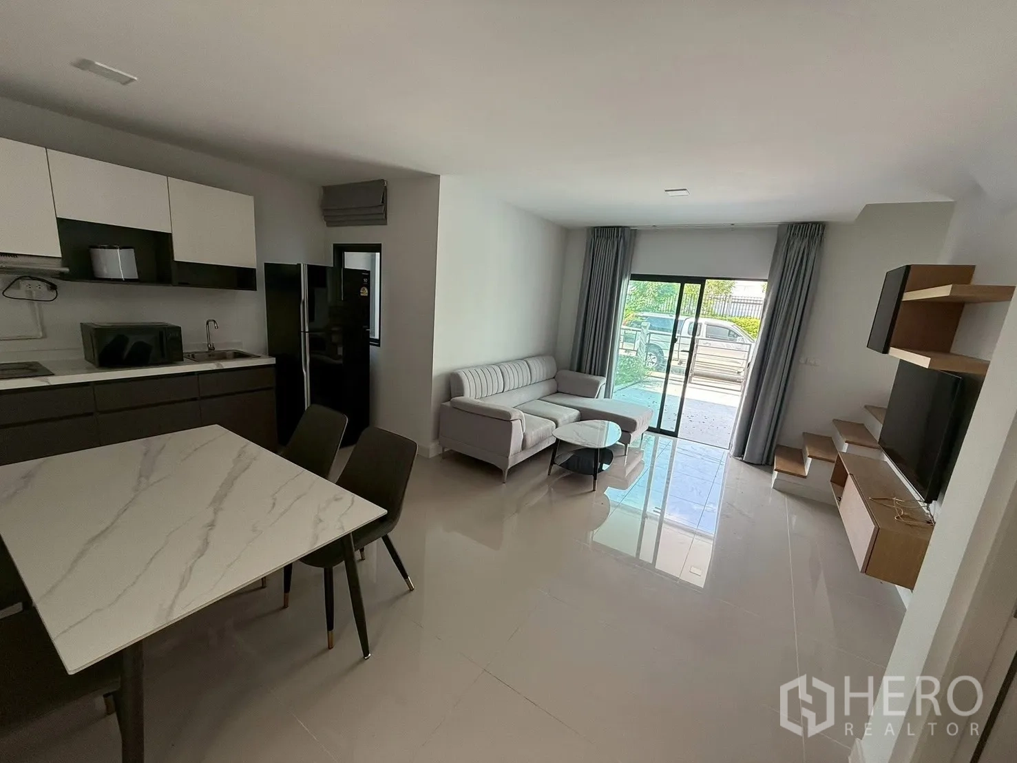 Townhouse for rent in Bang Phli, Samut Prakan - Living area with sofa, TV wall, kitchen and sliding doors to carport.