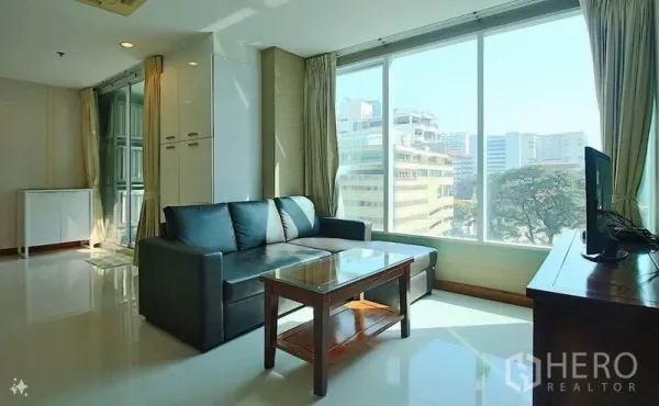 公寓 出售在Watthana, Bangkok - 明亮客厅，落地窗城市景观，黑色转角沙发与玻璃茶几。
