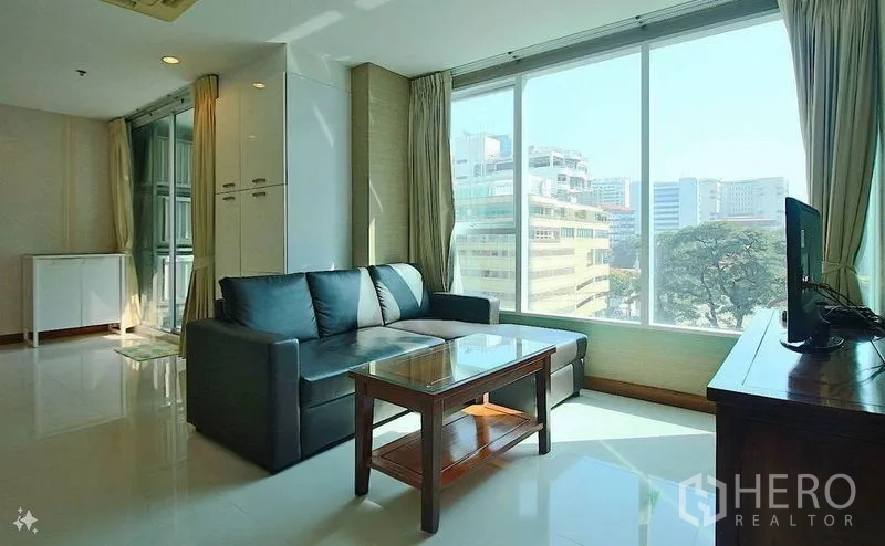 公寓 出售在Watthana, Bangkok - 明亮客厅，落地窗城市景观，黑色转角沙发与玻璃茶几。